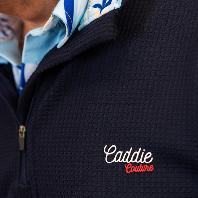 Navy golf jacket with 'Caddie Couture' logo on a blurred background