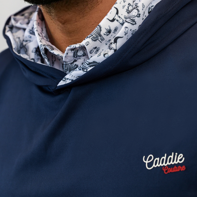 Navy blue golf hoodie with 'Caddie Couture' logo, worn over a patterned shirt.