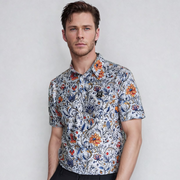 A man wearing a white short-sleeved golf polo with a vintage floral design in blue, orange, and green colors.