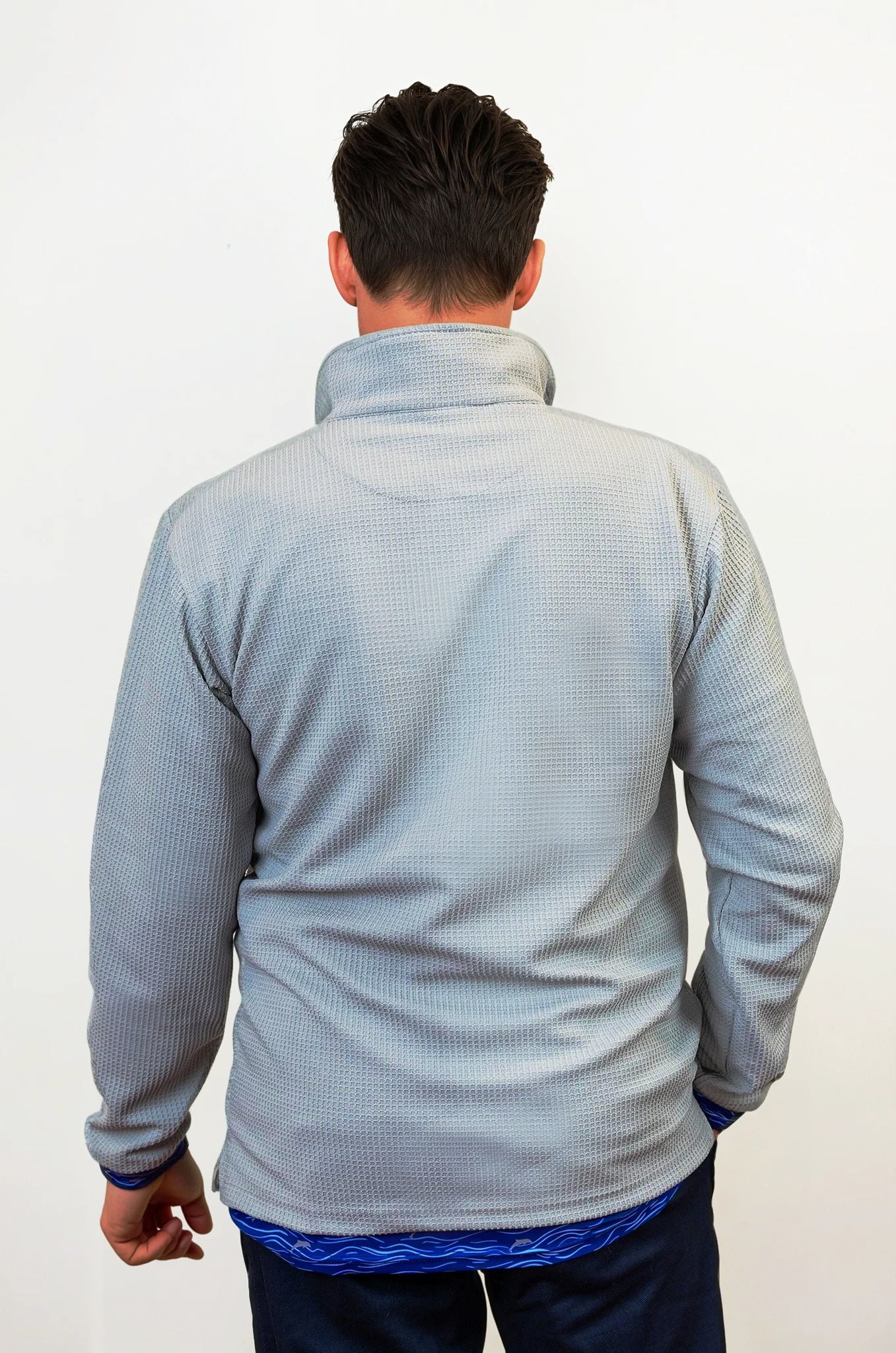Person wearing a light gray textured sweater over a blue shirt with a white background