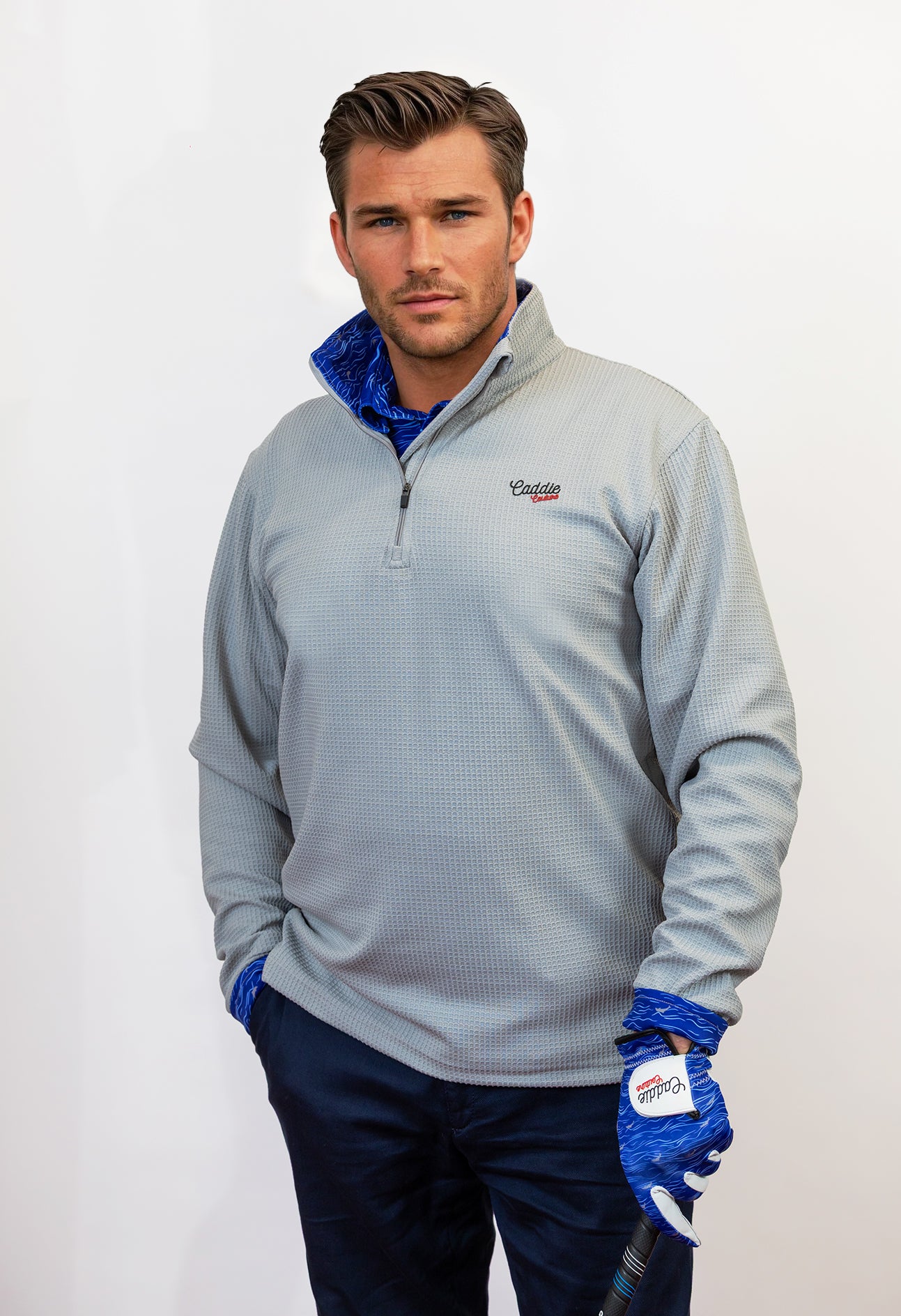 Man wearing golf quarter zip with blue wave pattern in neck. Holding Golf club with matching glove
