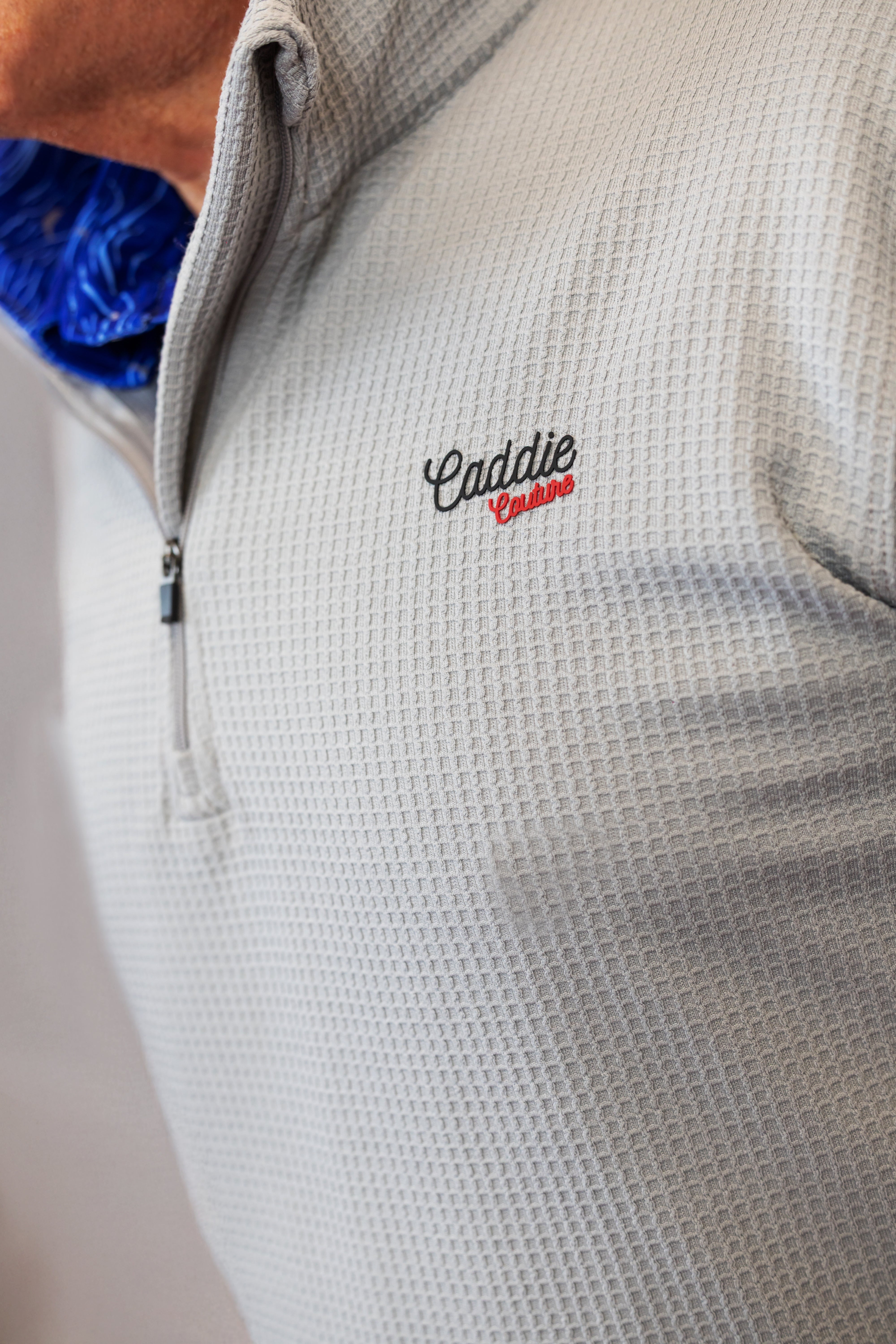 Close-up of a textured gray jacket with 'Caddie Couture' embroidery on a neutral background