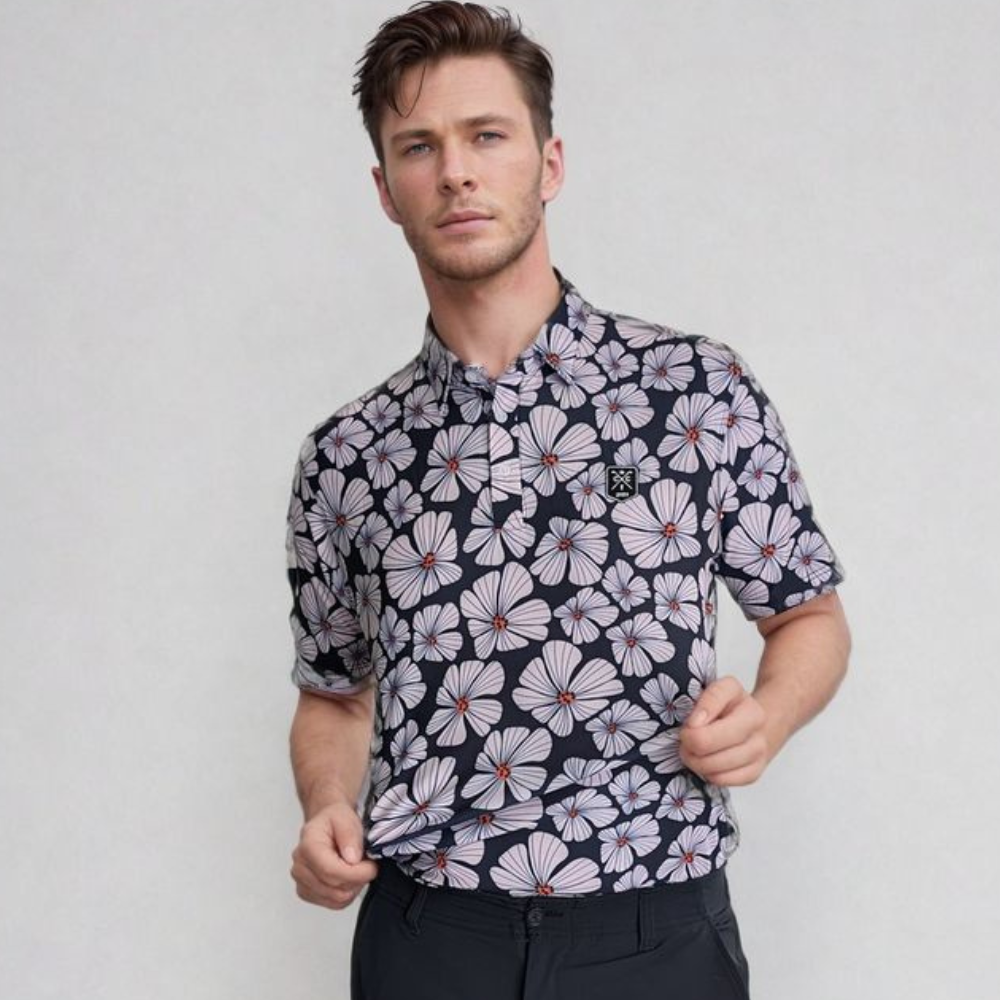 A man wearing a black golf polo with a floral pattern consisting of pink and white flowers and green leaves.