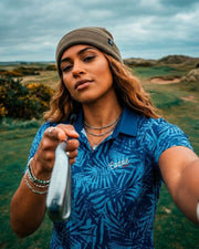 Woman in a blue patterned shirt holding a golf club outdoors