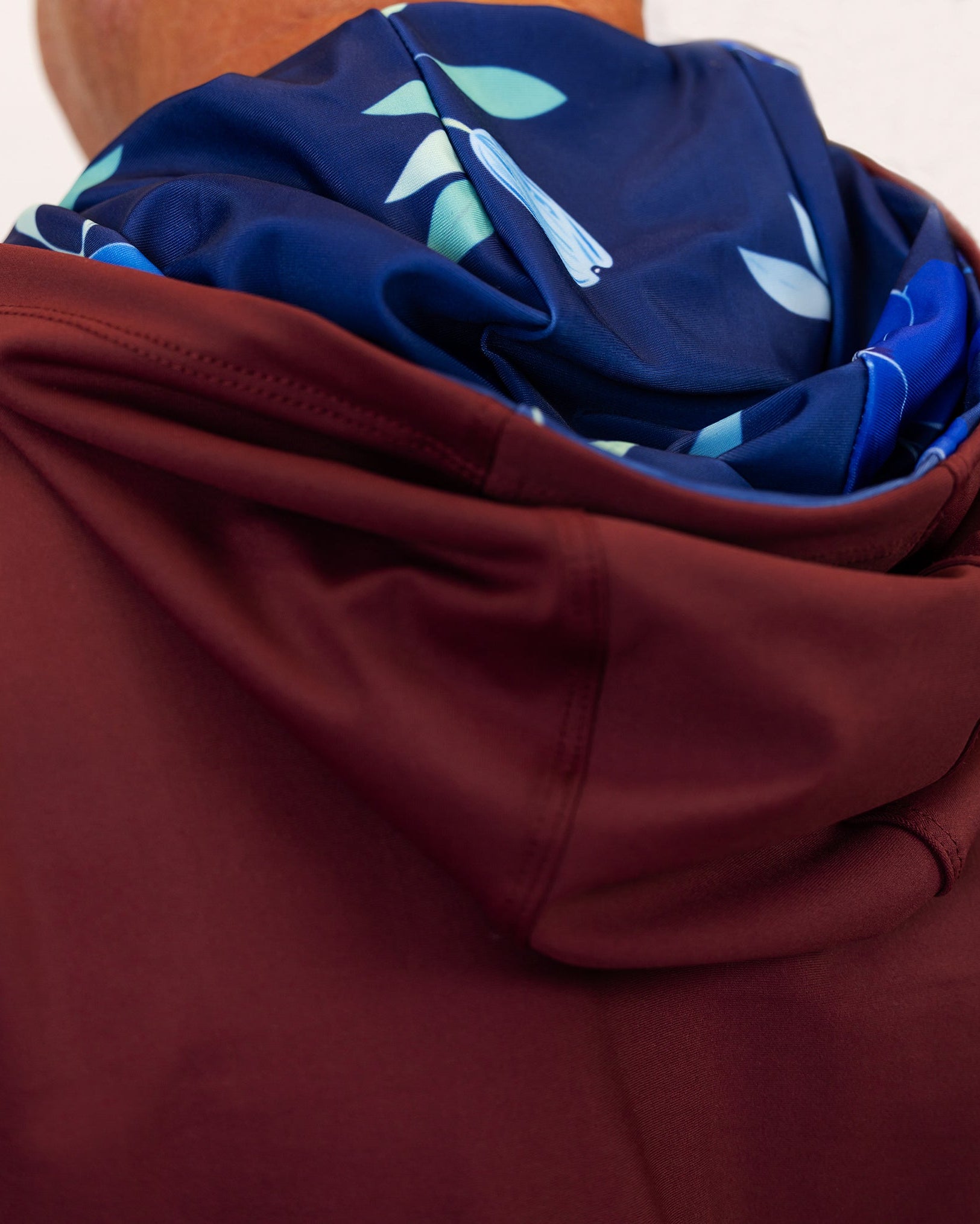 Close-up of a maroon golf hoodie with a folded navy fabric with leaf patterns on top.