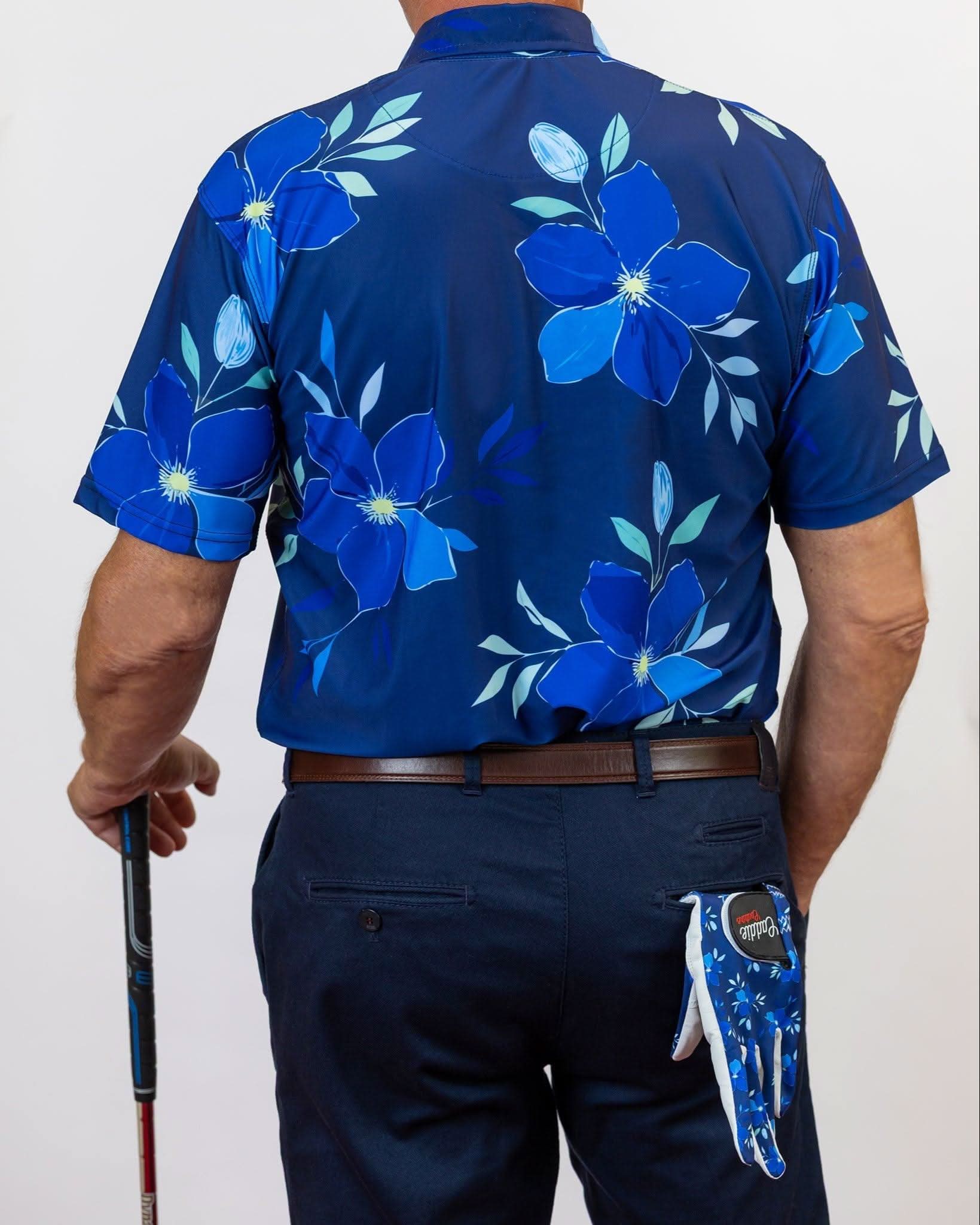Person wearing a blue floral golf shirt with a white background. with a golf glove hanging out of his back pocket.