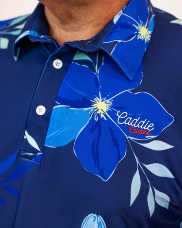 Navy blue polo golf shirt with floral design and 'Caddie Couture' branding.