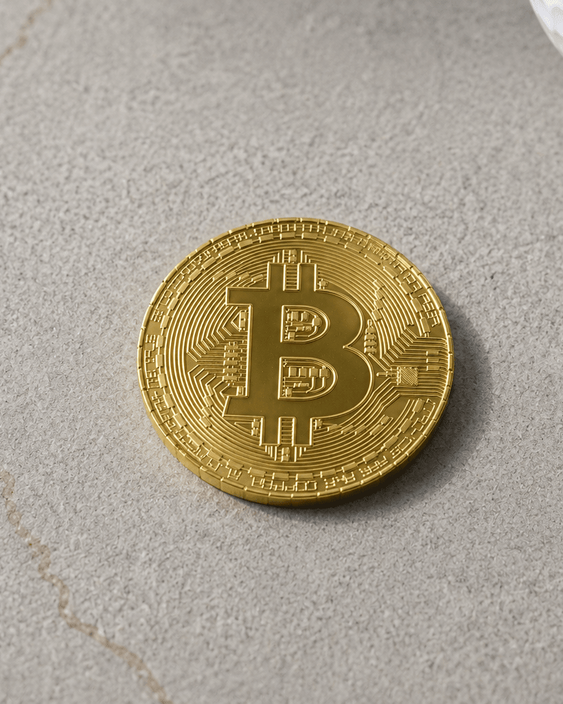 Gold Bitcoin coin on a gray surface with a golf ball in the background