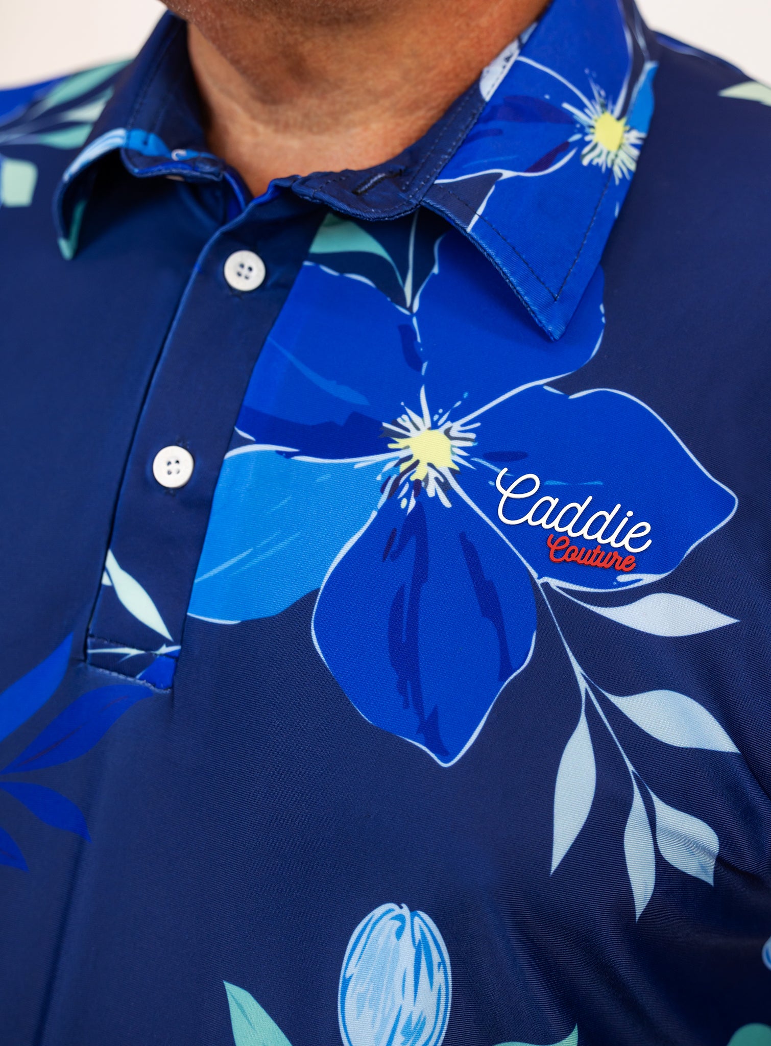 Navy blue polo golf shirt with floral design and 'Caddie Couture' branding.