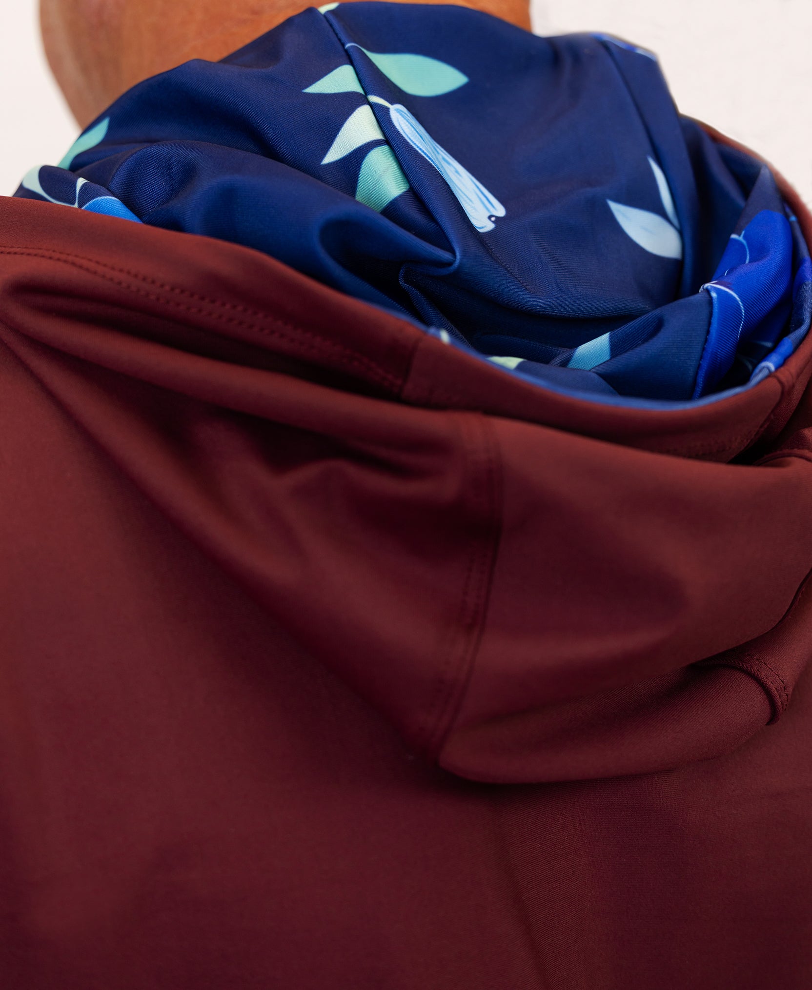 Close-up of a maroon golf hoodie with a folded navy fabric with leaf patterns on top.
