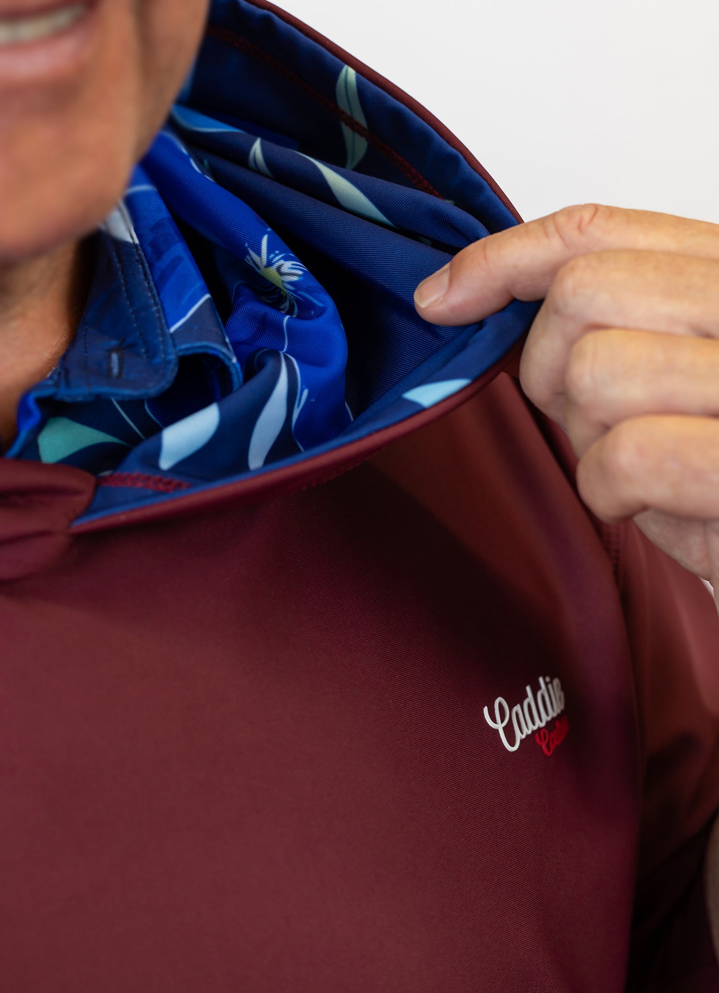 Person wearing a maroon golf hoodie with a blue lining, featuring a visible brand logo.