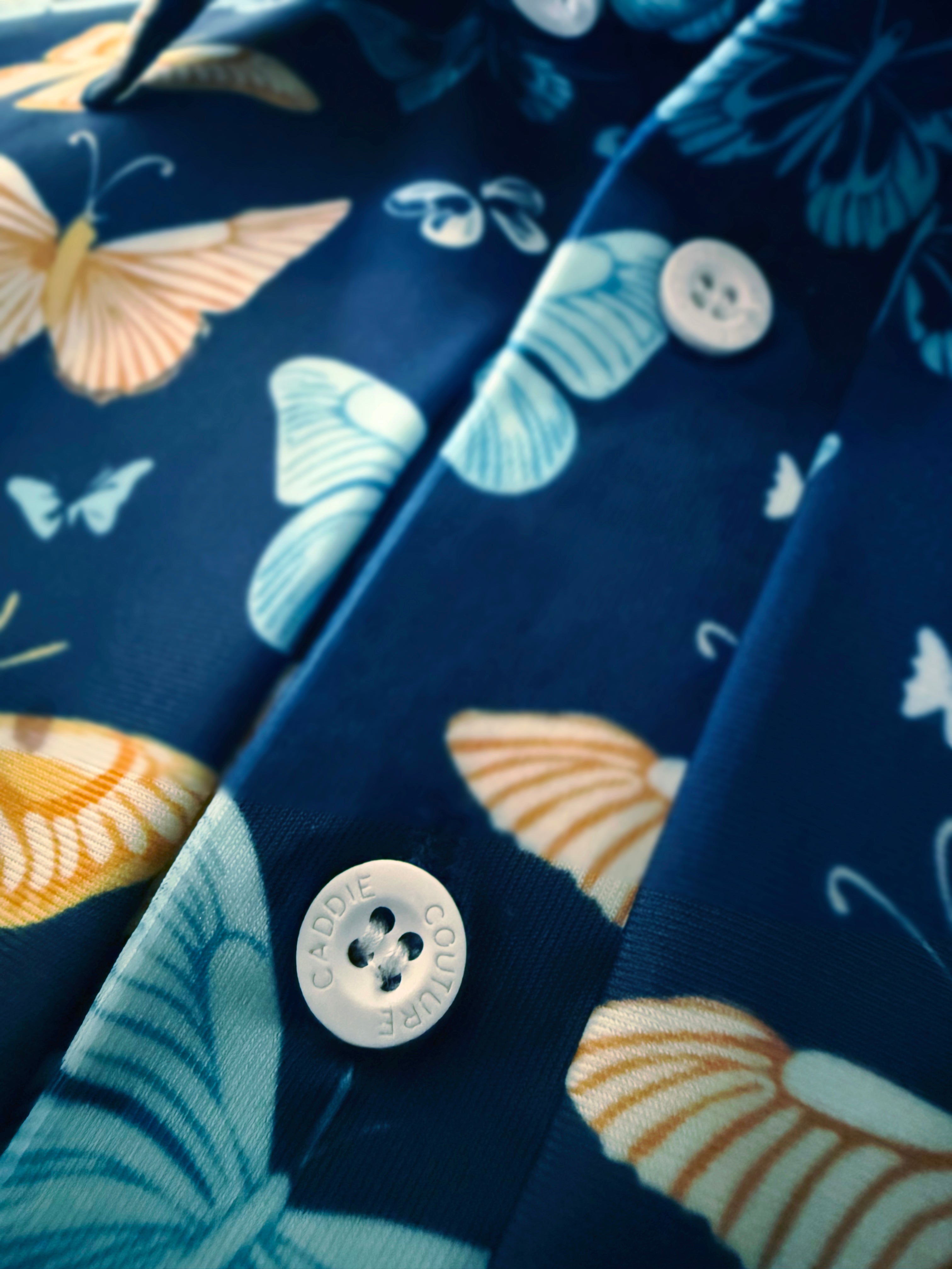 Close-up of a golf polo with butterfly pattern and button, featuring the brand 'Caddie Couture"