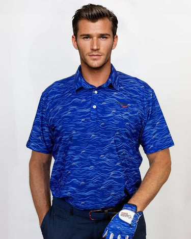 Man wearing a blue patterned golf polo shirt and navy pants, holding a golf club on a white background