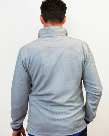 Person wearing a light gray textured sweater over a blue shirt with a white background