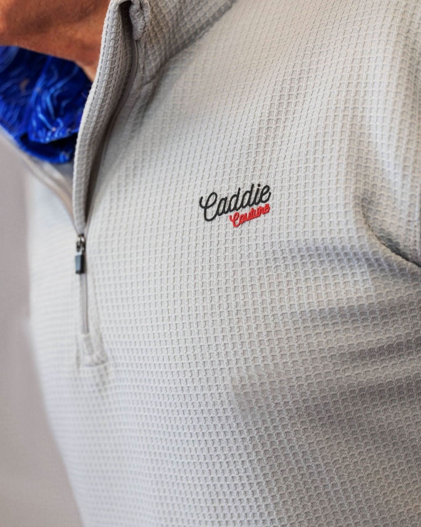 Close-up of a textured gray jacket with 'Caddie Couture' embroidery on a neutral background