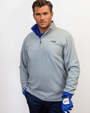 Man wearing golf quarter zip with blue wave pattern in neck. Holding Golf club with matching glove