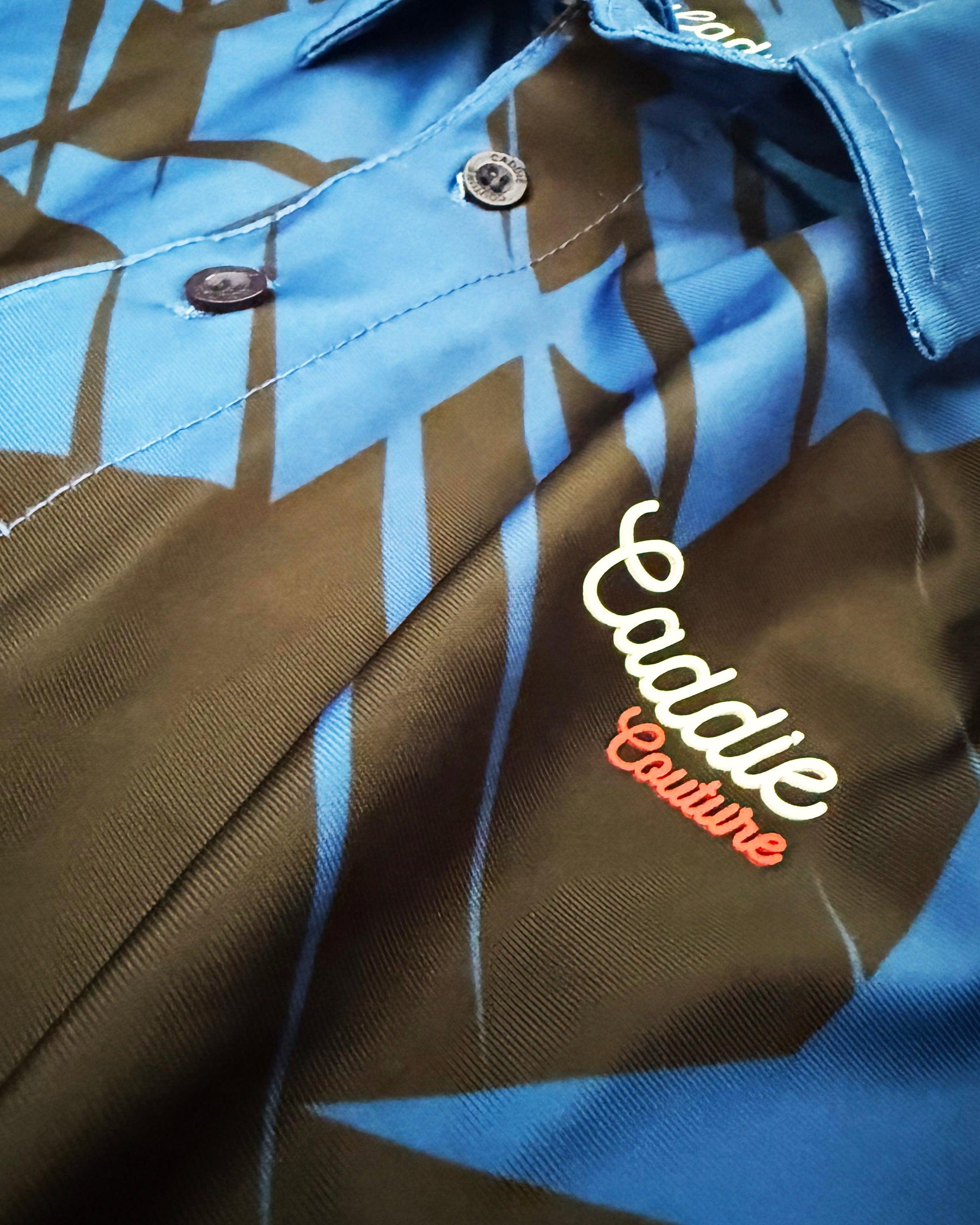 Close-up of a jacket with 'Caddie Couture' branding on a blue and brown patterned fabric.