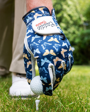 Golf glove with butterfly pattern holding a golf ball on grass