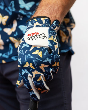Golf glove with butterfly pattern worn by a person, against a blurred background