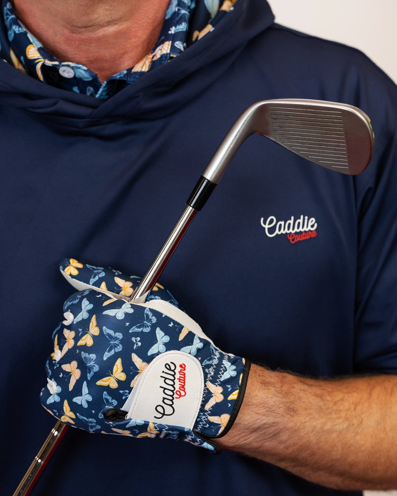 Person wearing a navy blue hoodie with 'Caddie' logo, holding a golf club and glove.
