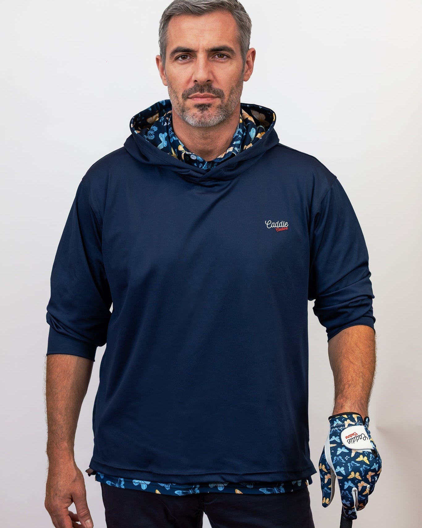 Man wearing a navy blue hoodie with a brand logo, holding a golf club and glove.