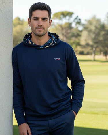 Man wearing a navy butterflies golf hoodie with a caddie couture logo, standing on a golf course.