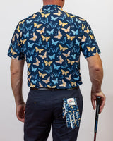 Person wearing a navy shirt with butterfly pattern, holding a golf club, on a plain background
