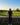 Person standing on a golf course looking over a green with trees and clear sky.