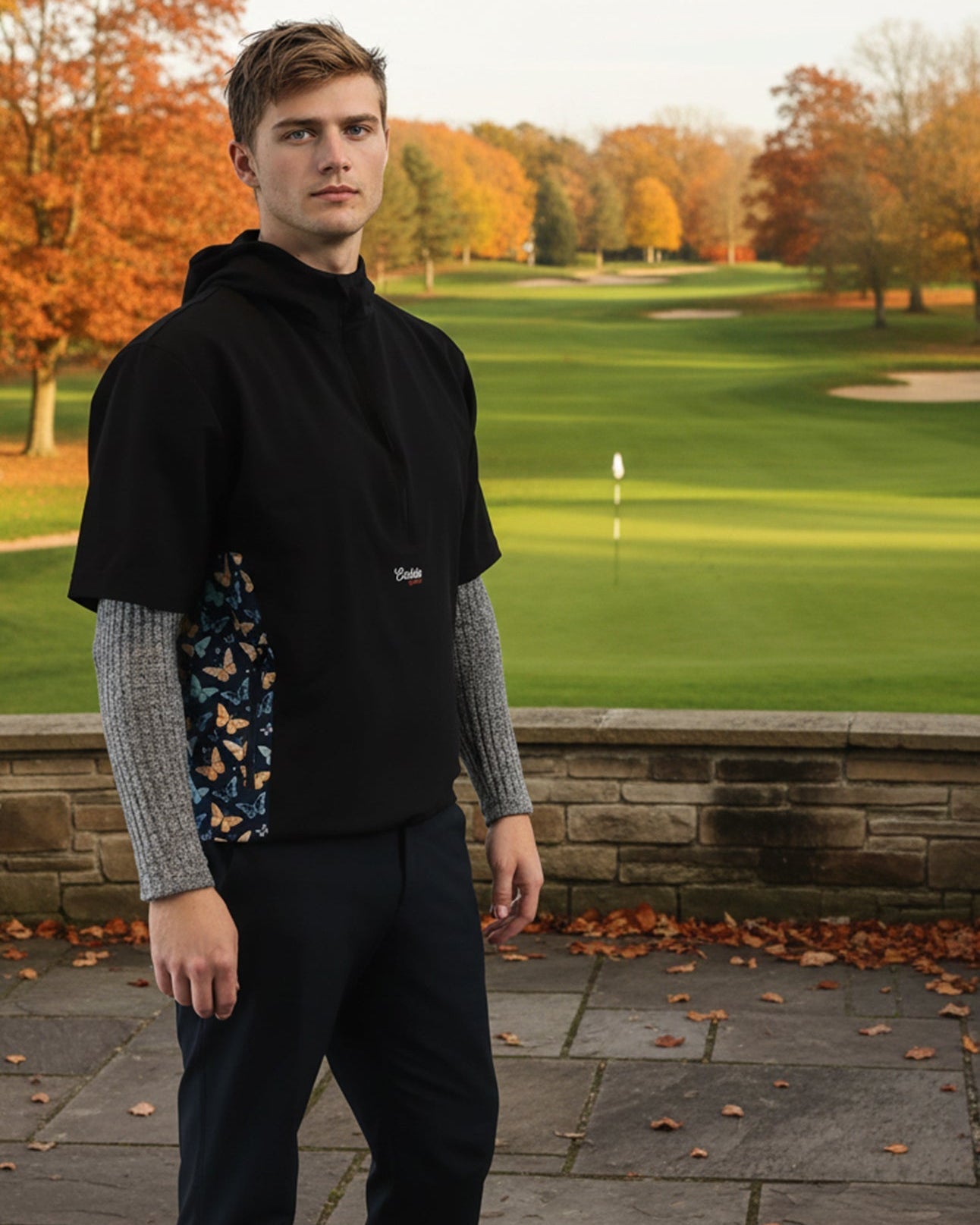 Man standing on a golf course wearing a black windbreaker jacket with a brand logo.