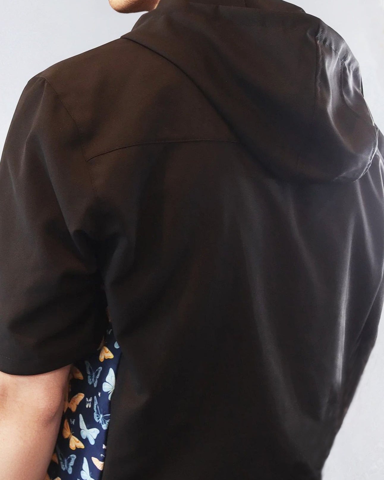 Person wearing a black windbreaker jacket with a butterfly patterned sides on a white background