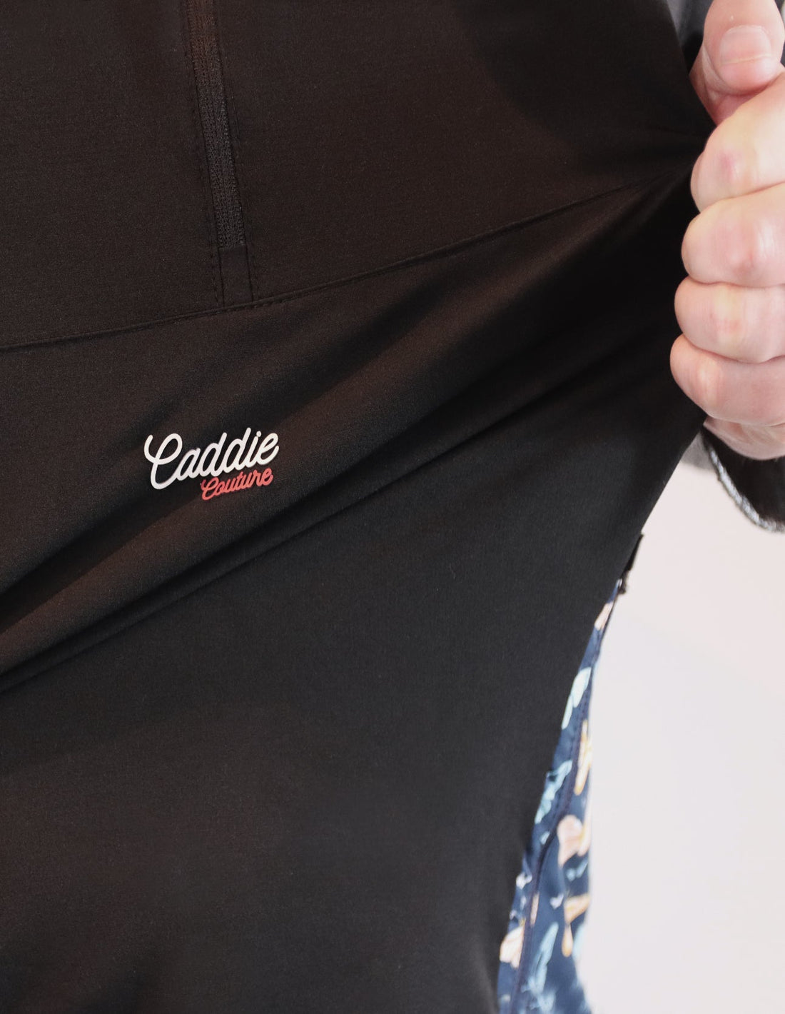 Close-up of a black jacket with 'Caddie' embroidery on a neutral background