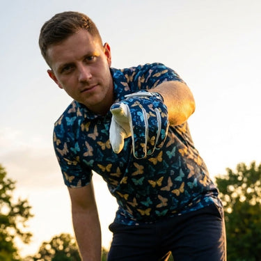Man in a blue shirt with butterfly pattern holding a golf club outdoors