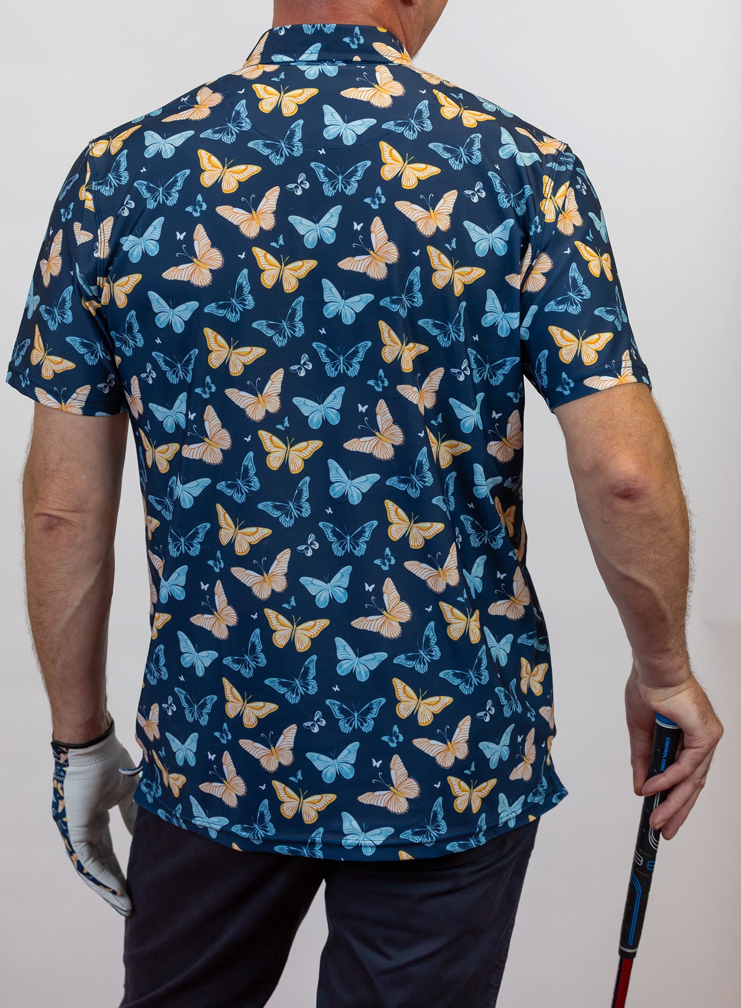 Person wearing a blue golf polo with butterfly pattern holding a golf club.