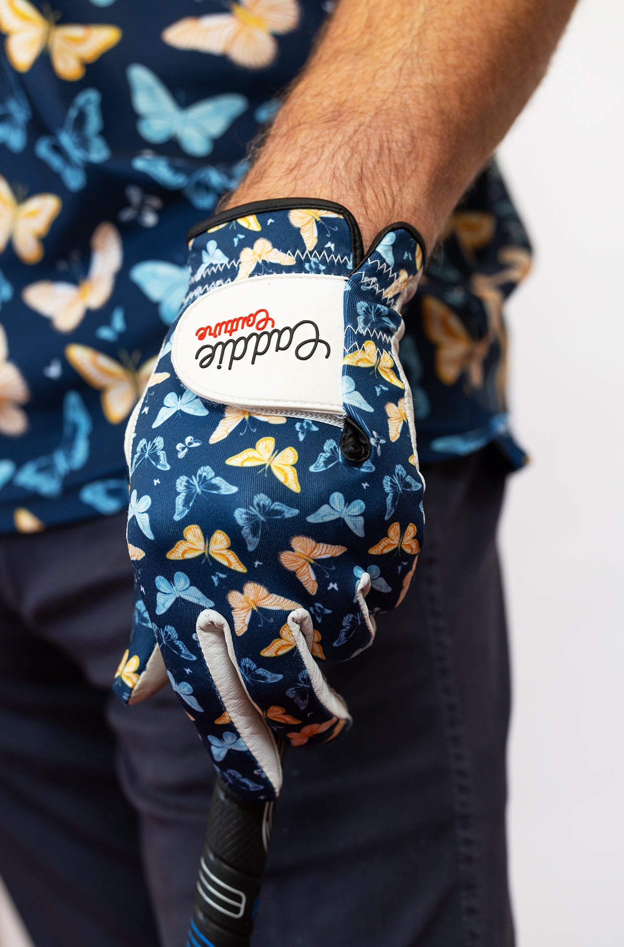 Golf glove with butterfly pattern worn by a person, against a blurred background