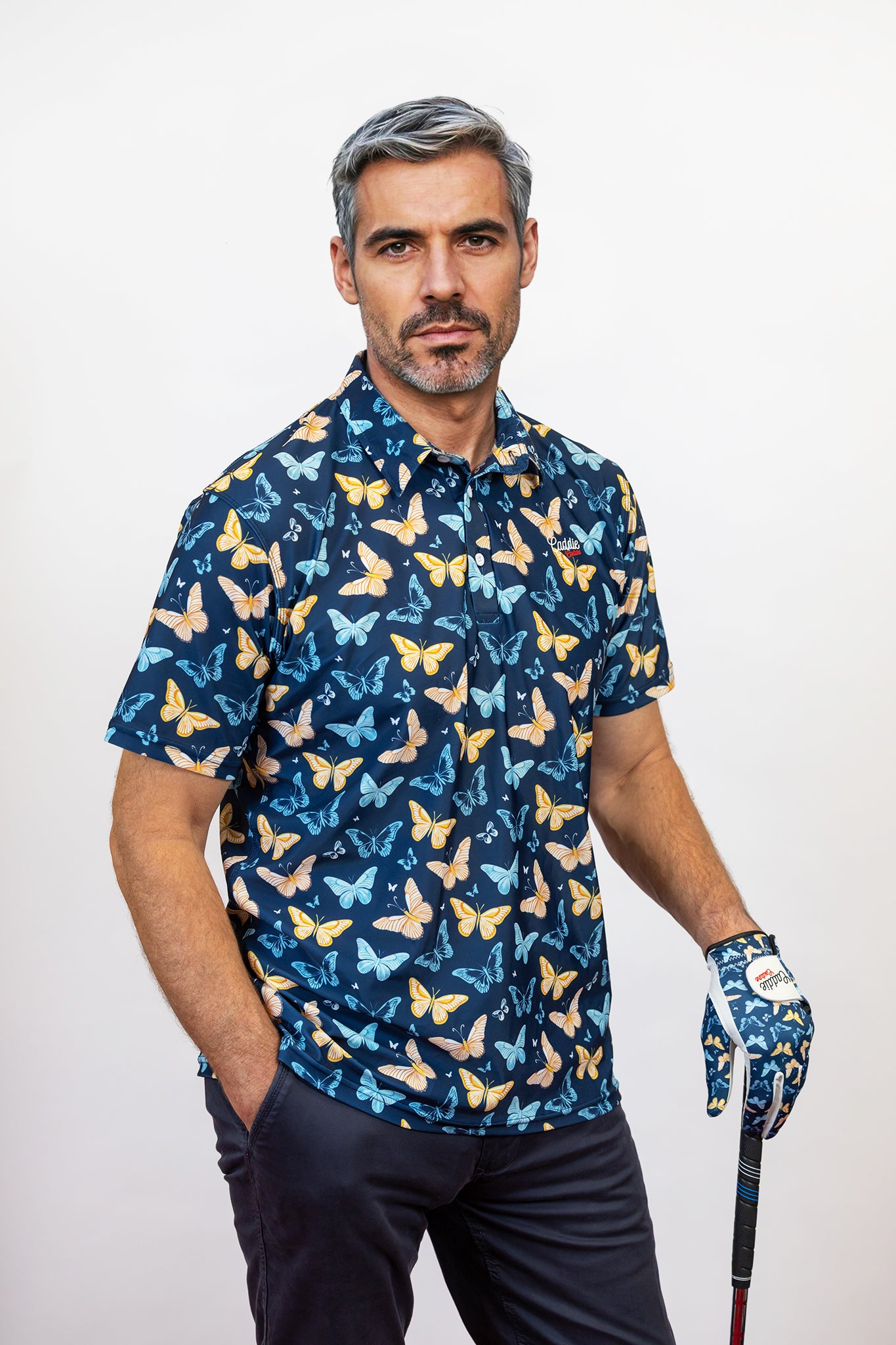 Man wearing a blue Golf Polo with butterfly pattern and holding a golf club on a white background