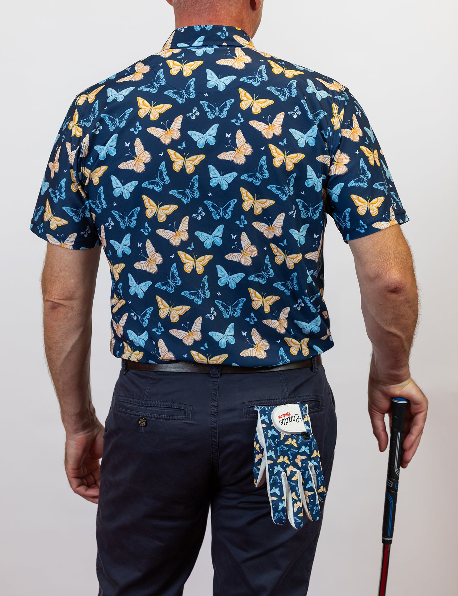 Person wearing a navy shirt with butterfly pattern, holding a golf club, on a plain background