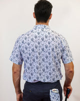 Man wearing a patterned shirt and navy pants, holding a golf club and glove, on a plain background