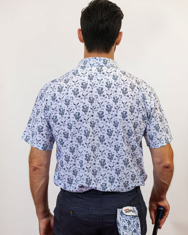 Man wearing a patterned shirt and navy pants, holding a golf club and glove, on a plain background