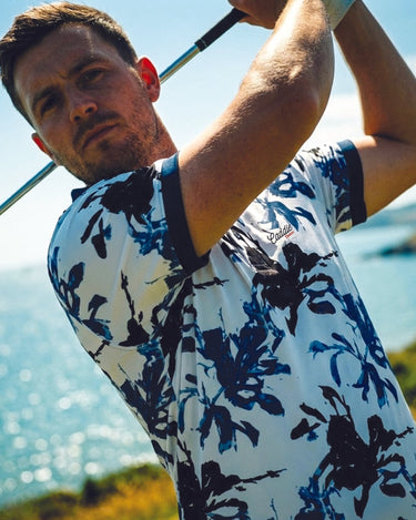 Man in a floral shirt swinging a golf club with a scenic background