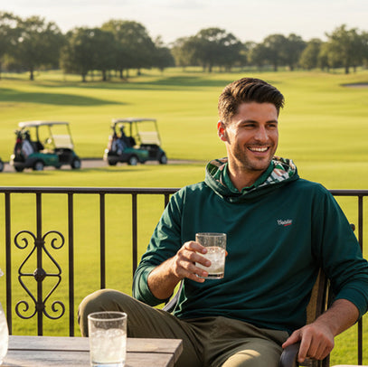 man having a drink, laughing on a golf course wearing green golf hoodie