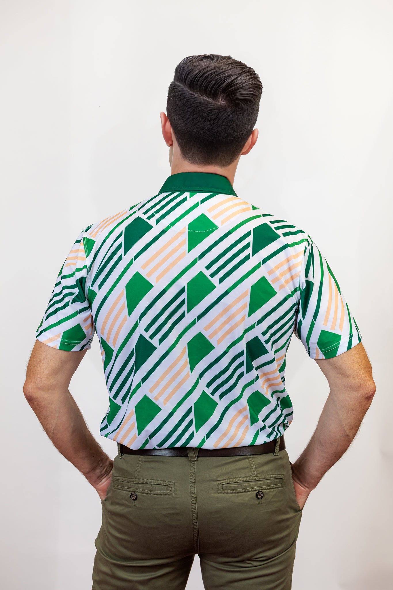 Man wearing a patterned golf shirt with green, white design on a plain background