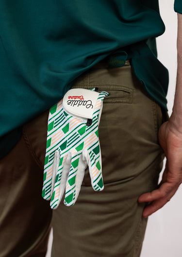 White and green patterned glove held by a person wearing a green shirt and brown pants.