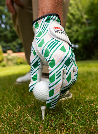 Golf glove with green and white pattern holding a golf ball on grass