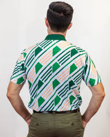 Man wearing a patterned golf shirt with green, white design on a plain background