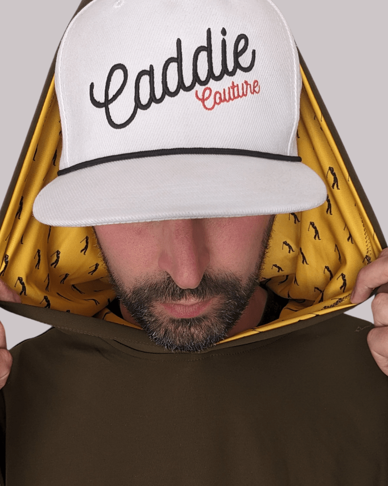 A person wearing a white golf hoodie with 'Caddie Couture' written on the cap in red. The hoodie has an olive green body with yellow golfer design details.
