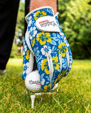 Golf glove with floral design holding a golf ball on a tee in a grassy area