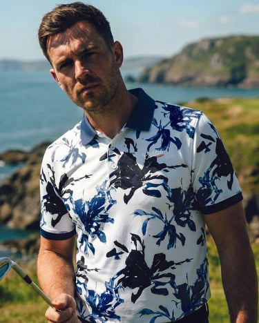 Man in a floral polo shirt holding a golf club with a scenic background