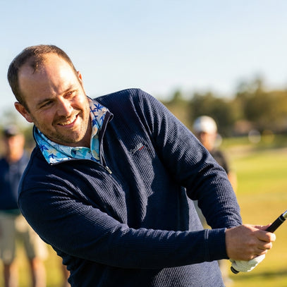 Man playing golf on a sunny day with green grass and blue sky.