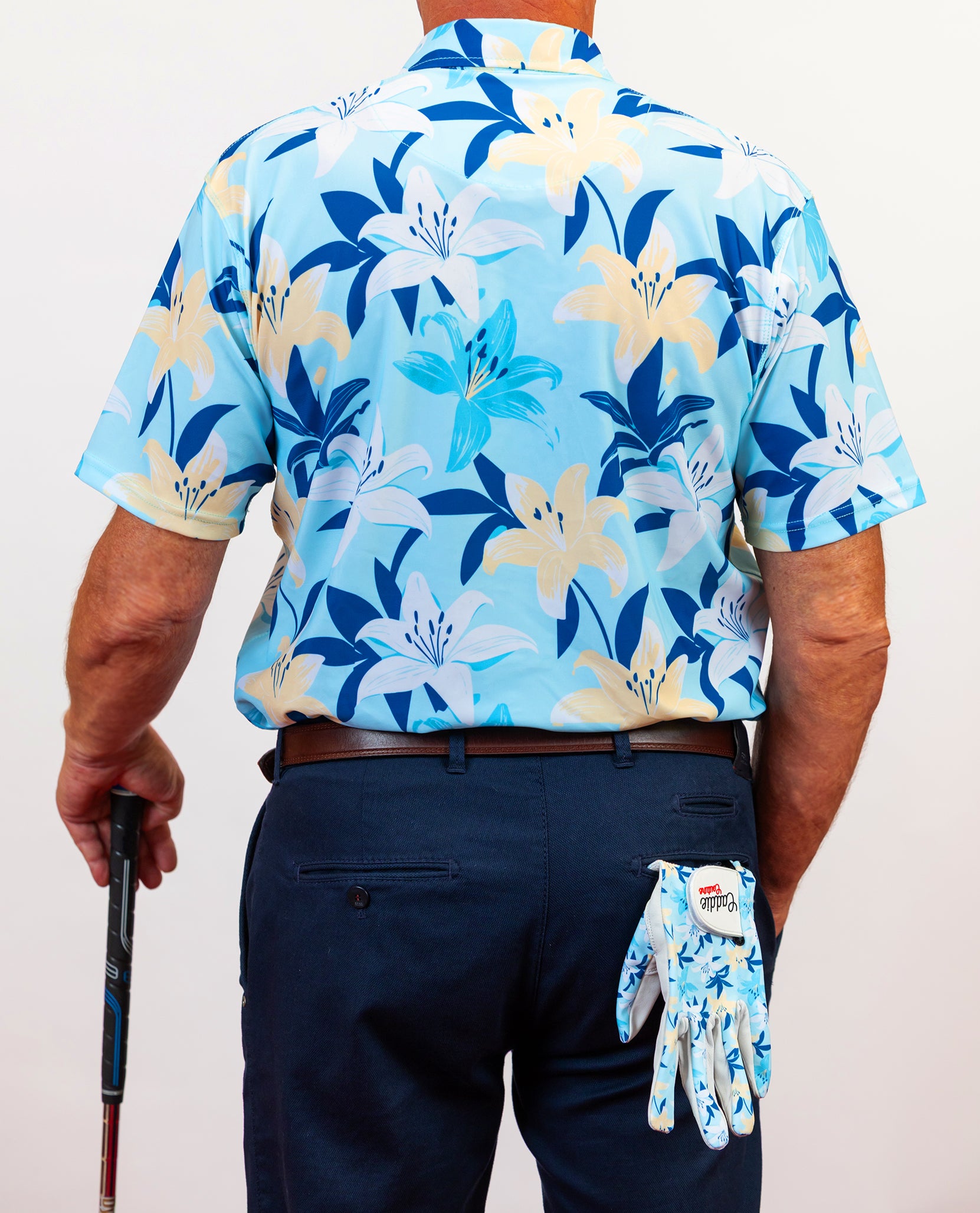 Person wearing a blue floral golf shirt and holding a golf glove with a brand logo caddie couture.