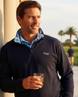 Man wearing caddie couture qzip, holding a glass, standing outdoors.
